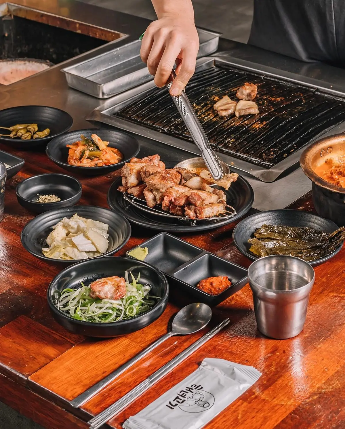 Staff plating grilled pork at Haenyeo Gogi beside a tabletop grill and side dishes.