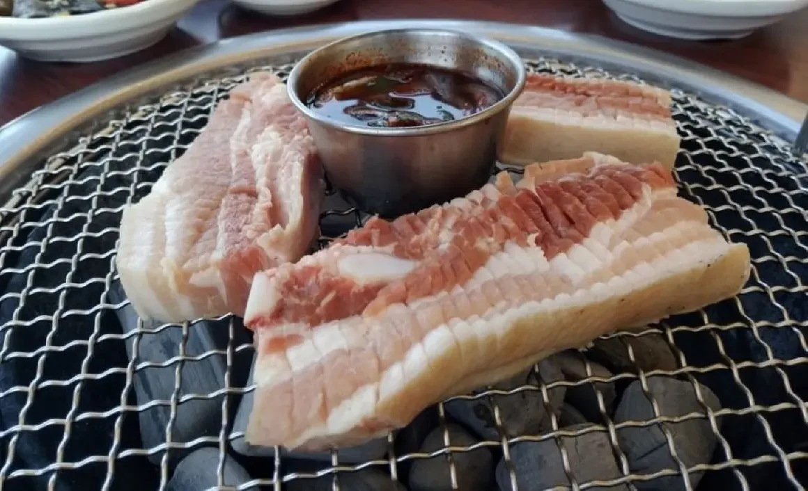 Historical thick-cut pork and sauce on a grill at Neulbom Black Pork.