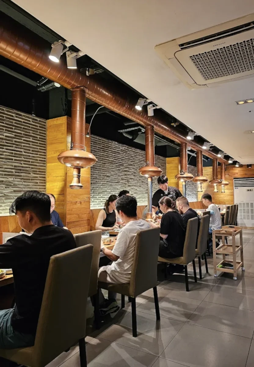 Wangbijib Central dining room with tabletop grills and copper exhaust hoods; photograph date unknown.